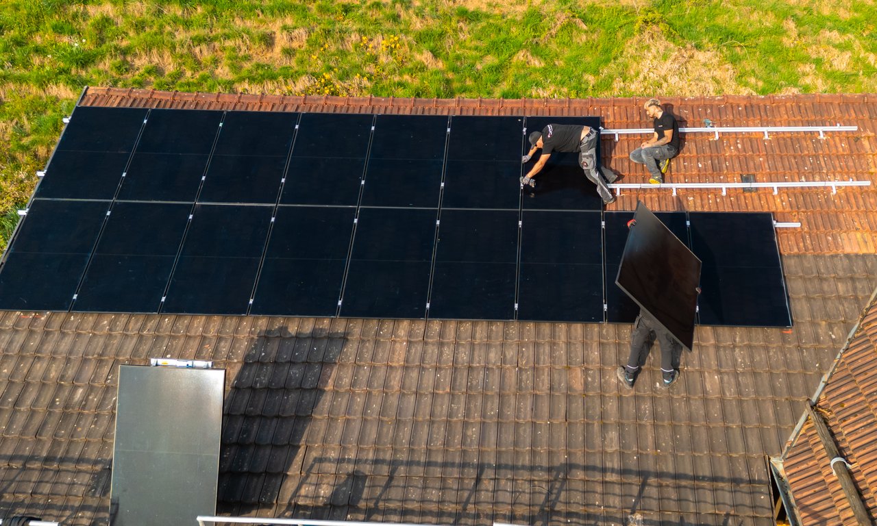 AlpenEnergie-Mitarbeiter montieren Solarmodule auf einem Ziegeldach