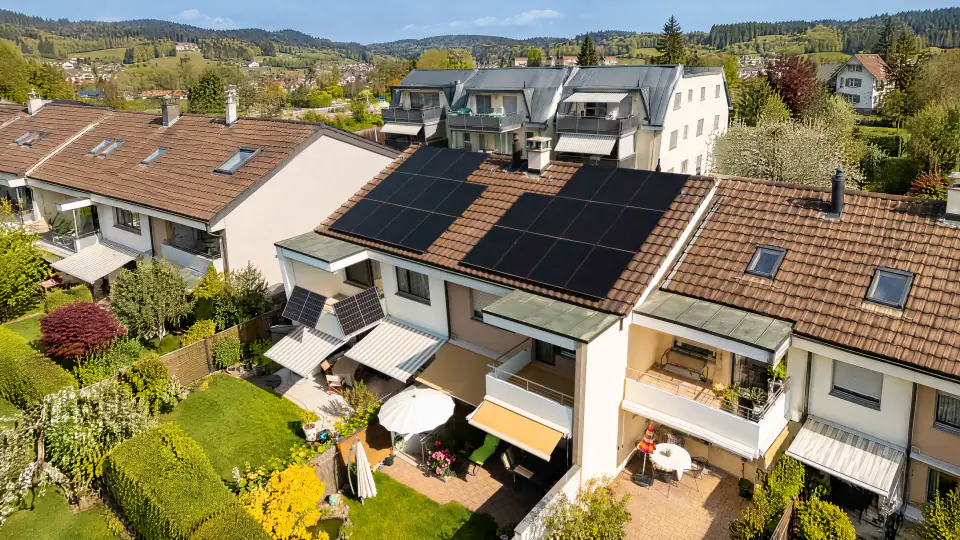 Reihenhaus mit schwarzen Solarmodulen auf dem Ziegeldach und zwei Balkonmodulen, Gärten auf der Rückseite