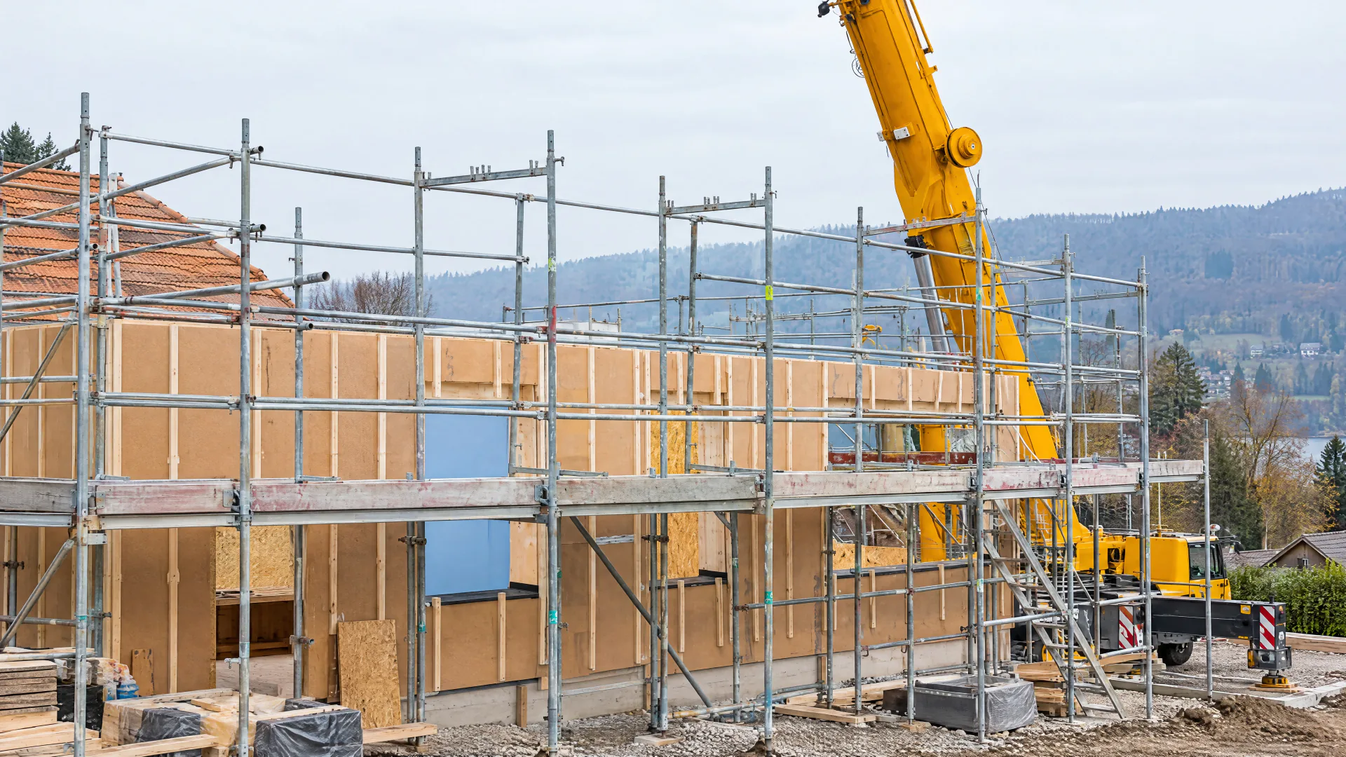 Holzbau während der Sanierung mit Holzfaser-Dämmplatten hinter einem Baugerüst, daneben ein gelber Autokran