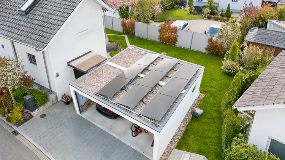 Carport mit Kiesdach und acht aufgeständerten Solarmodulen neben einem Einfamilienhaus, Drohnenblick von oben