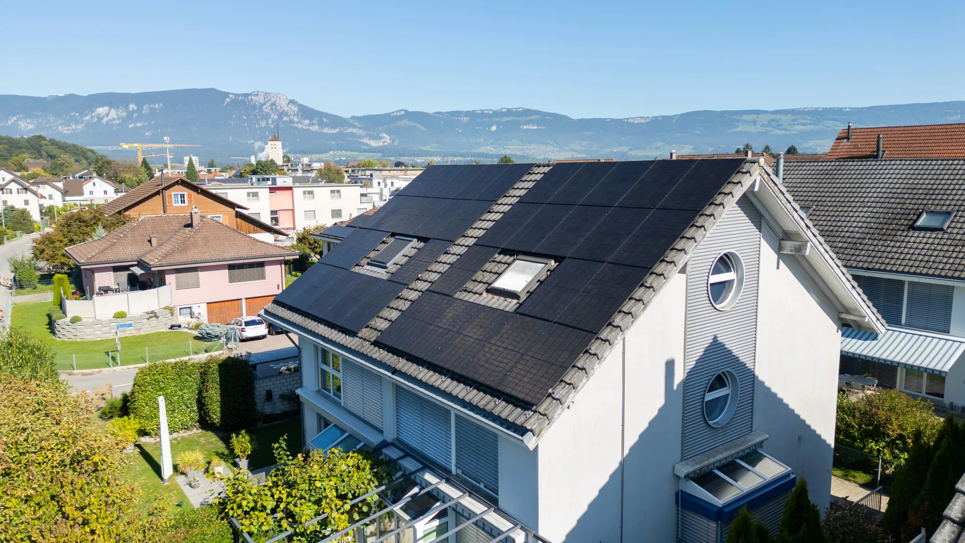 Solarmodule über die ganze Dachseite eines weissen Wohnhauses, im Hintergrund die Jurakette