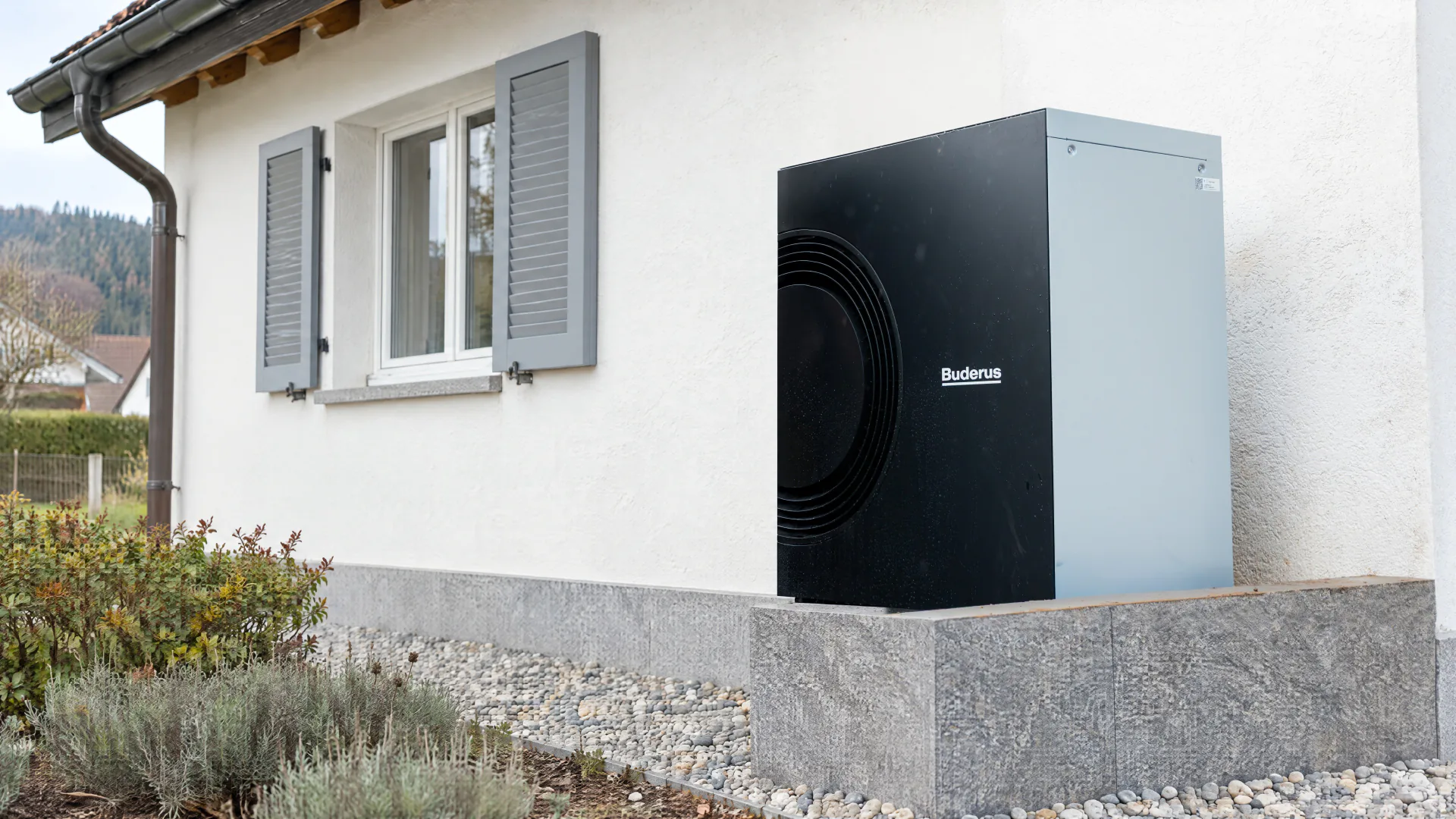 Luft-Wasser-Wärmepumpe auf einem Granitsockel an der weiss verputzten Hauswand eines Einfamilienhauses