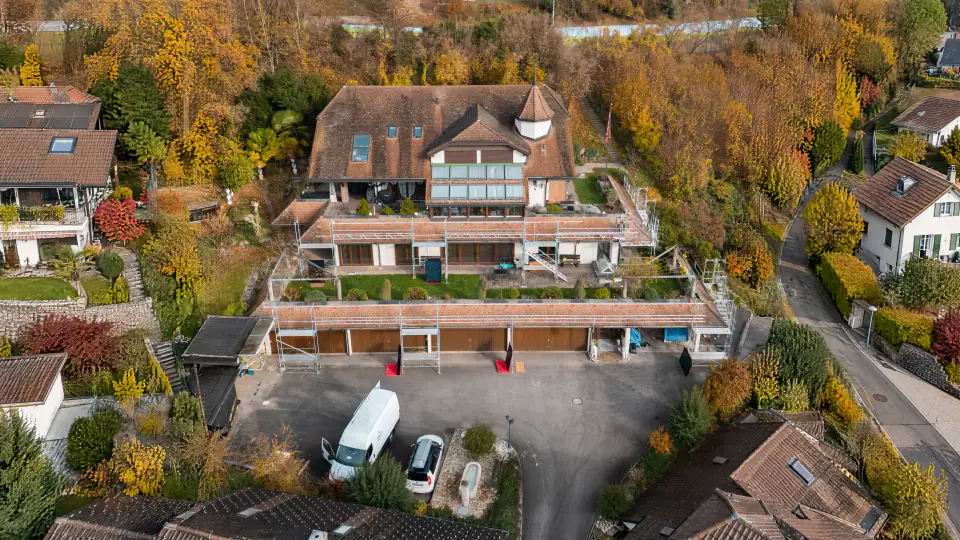 Terrassenhaus am Hang mit Gerüsten auf allen Dachstufen während der Montage, Drohnenblick im Herbst