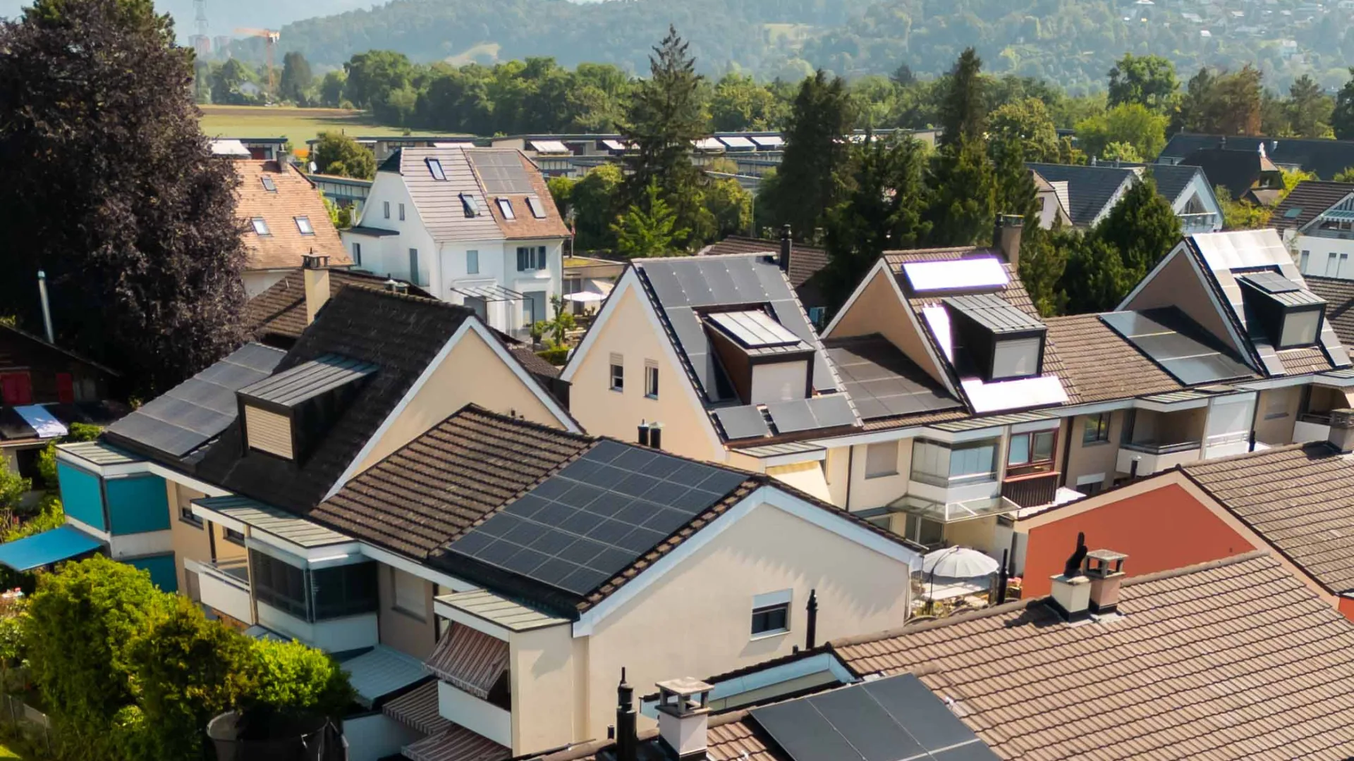 Reihenhausquartier mit Solaranlagen auf mehreren Nachbardächern, Drohnenblick über die Dächer bis zu den Hügeln